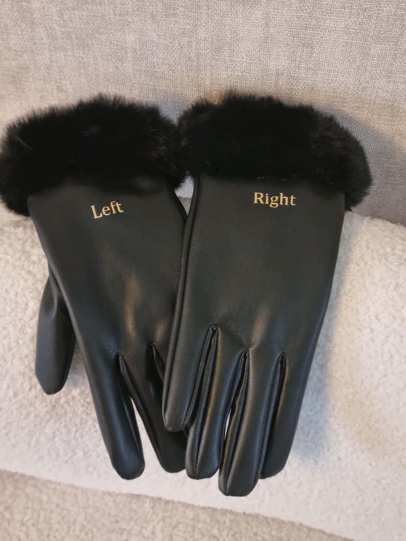 May include: A pair of black gloves featuring a smooth finish and black fur trim at the cuffs. The left glove has the word Left printed in gold lettering, and the right glove has the word Right printed in gold lettering on the back of the hand.
