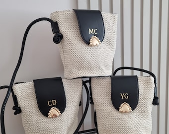 May include: Three woven straw bucket bags with black leather flaps. Each bag has a gold heart-shaped clasp and a strap. The bags are personalized with the initials "MC", "CD", and "YG" in gold lettering.