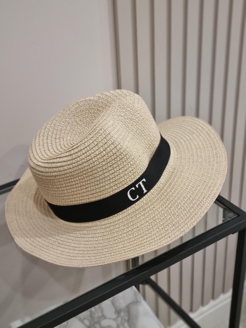 May include: A beige straw hat with a black ribbon and the initials "CT" embroidered in white.