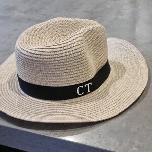 May include: A beige straw hat with a black band and the initials "CT" embroidered in white.