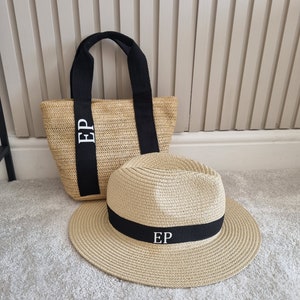 May include: A straw tote bag and a straw hat with black ribbon trim. Both items have the initials "EP" embroidered in white.