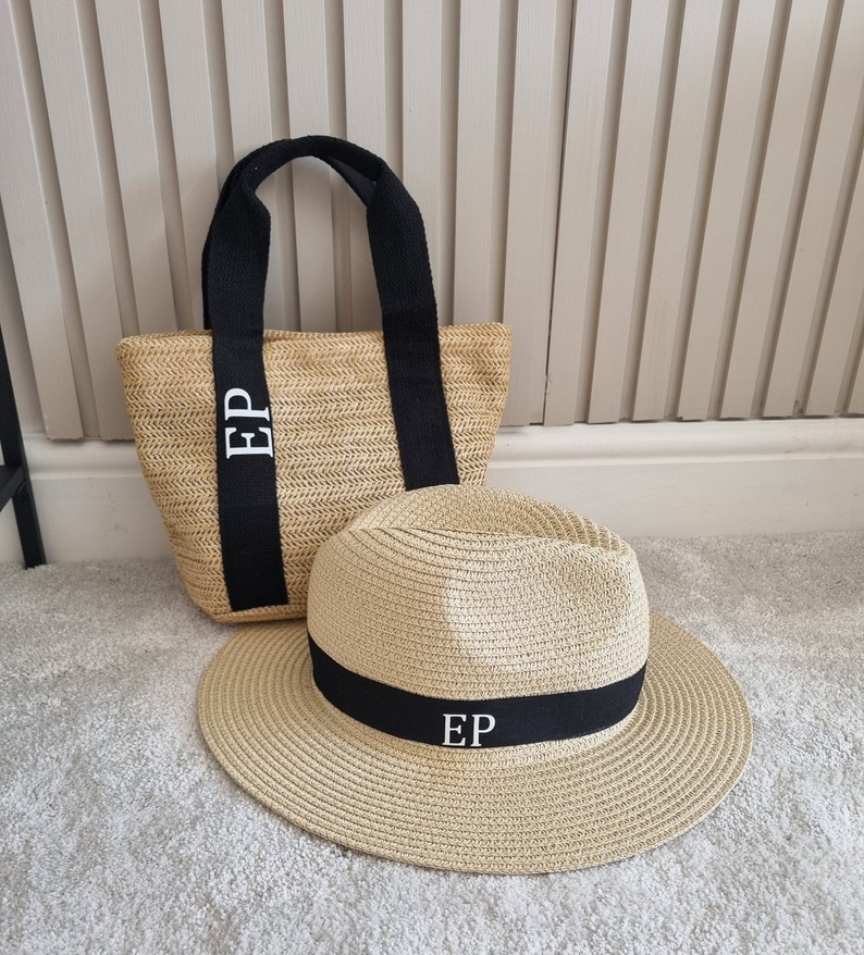 May include: A straw tote bag and a straw hat with black ribbon trim. Both items have the initials "EP" embroidered in white.