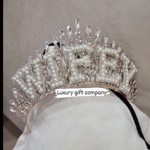 May include: A gold-tone headband with the word "WIFEY" spelled out in white pearls and rhinestones. The headband is decorated with a crown of smaller rhinestones.