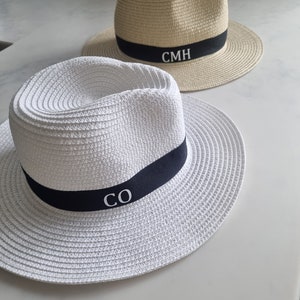 May include: Two straw hats with black bands. The hat on the left is white with the initials "CO" embroidered on the band. The hat on the right is beige with the initials "CMH" embroidered on the band.