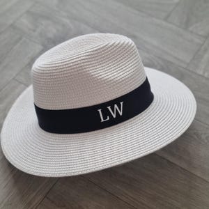 May include: A white straw hat with a black band and the initials "LW" embroidered in white.