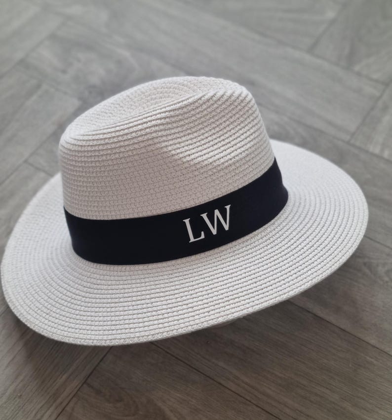 May include: A white straw hat with a black band and the initials "LW" embroidered in white.