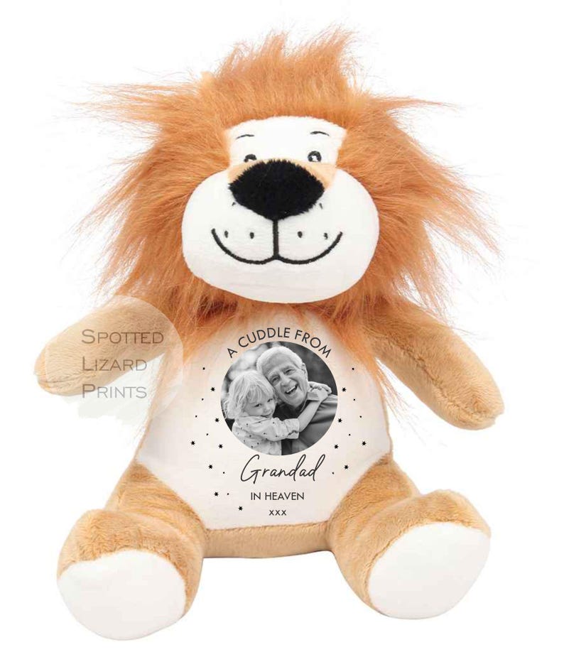 May include: A plush lion toy with tan fur, a white face, and a brown mane. The chest features a circular design with a black and white photograph of a child and an adult, the text A CUDDLE FROM, Grandad, IN HEAVEN, xxx, and small stars.