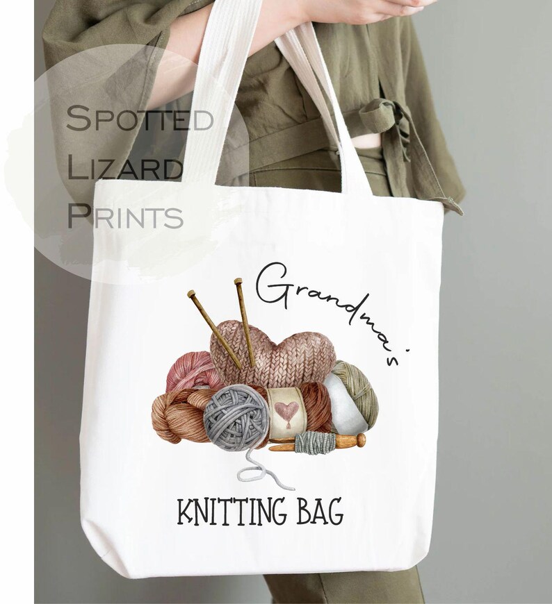 May include: White tote bag with a colorful knitting design. The bag features a heart-shaped knitted item, yarn balls, knitting needles, and the words "Grandma's Knitting Bag". The bag is held by a person.