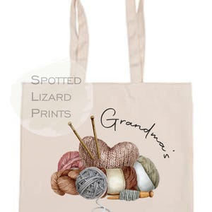 May include: Beige tote bag with a watercolor illustration of yarn balls, knitting needles, and a knitted heart. The text "Grandma's Knitting Bag" is printed on the bag.