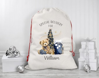 Könnte beinhalten: Ein großer weißer Weihnachtsgeschenksack mit rotem Kordelzug. Der Beutel zeigt eine Aquarellillustration eines Teddybären, eines Weihnachtsbaums und Geschenken. Der Text auf der Tasche lautet "Special Delivery For William."