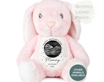 May include: A soft pink plush rabbit toy featuring a white circular patch on its chest. The patch displays a black and white ultrasound image, the text "HAPPY MOTHER'S DAY", "Mummy", "LOVE BUMP", and "2027". Text in the image includes "SPOTTED LIZARD PRINTS".