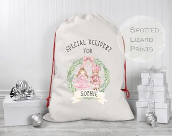 Puede incluir: Una bolsa de regalo grande de lona blanquecina con cierre de cordón rojo. La bolsa presenta una ilustración de acuarela de una niña y un cascanueces, con el texto "SPECIAL DELIVERY FOR SOPHIE". La bolsa está decorada con una corona y un lazo.