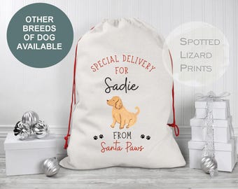 Może przedstawiać: Biały worek prezentowy z tkaniny z czerwonymi sznurkami i nadrukowanym tekstem SPECIAL DELIVERY FOR Sadie FROM Santa Paws, któremu towarzyszy graficzna ilustracja jasnobrązowego psa oraz małe czarne odciski łap z przodu.