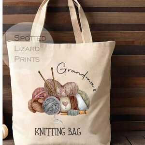 May include: Cream-colored tote bag with a watercolor illustration of yarn balls, knitting needles, and the words "Grandma's Knitting Bag." The bag has two handles and the text "Spotted Lizard Prints" in a circle.