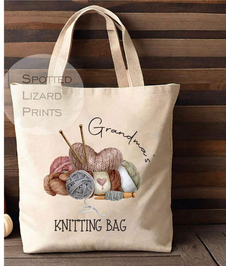 May include: Cream-colored tote bag with a watercolor illustration of yarn balls, knitting needles, and the words "Grandma's Knitting Bag." The bag has two handles and the text "Spotted Lizard Prints" in a circle.