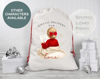 Puede incluir: Bolsa de regalo de lona blanca con cordón y ribete rojos, con una ilustración infantil. La ilustración muestra a una niña con un suéter rojo leyendo una lista, con el texto "Special Delivery For Evie". Estrellas decorativas y un lazo completan el diseño.