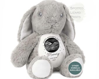 May include: A plush gray rabbit with long ears and white foot pads. A white circular patch on the chest features a black and white ultrasound image, the text HAPPY MOTHER'S DAY, Mummy, LOVE BUMP, and 2027, surrounded by small black dots.