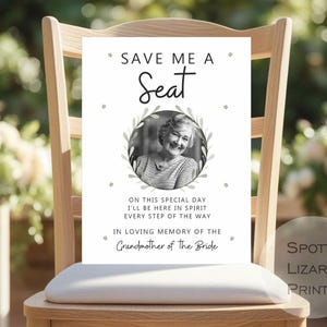 Op de afbeelding: Een wit bord met de tekst "SAVE ME A Seat" en een foto van een vrouw in een cirkelvormige lijst. Het bord bevat de tekst "ON THIS SPECIAL DAY I'LL BE HERE IN SPIRIT EVERY STEP OF THE WAY IN LOVING MEMORY OF THE Grandmother of the Bride."