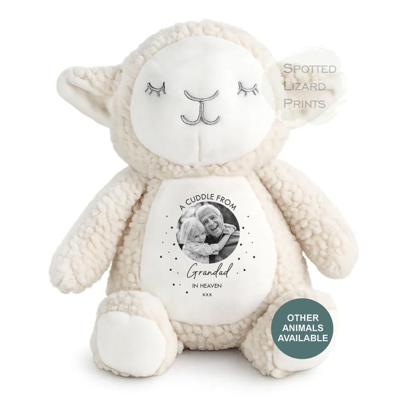 May include: A cream-colored plush lamb toy with a smooth white face and embroidered closed eyes. The belly features a circular black and white photograph of a child and an adult with the text A CUDDLE FROM GRANDAD IN HEAVEN xxx.