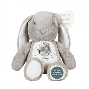 May include: A plush grey rabbit toy with long ears and white foot pads. The chest features a circular black and white photo of a person holding a baby, with the text A CUDDLE FROM Nanny IN HEAVEN xxx. The text SPOTTED LIZARD PRINTS appears above.