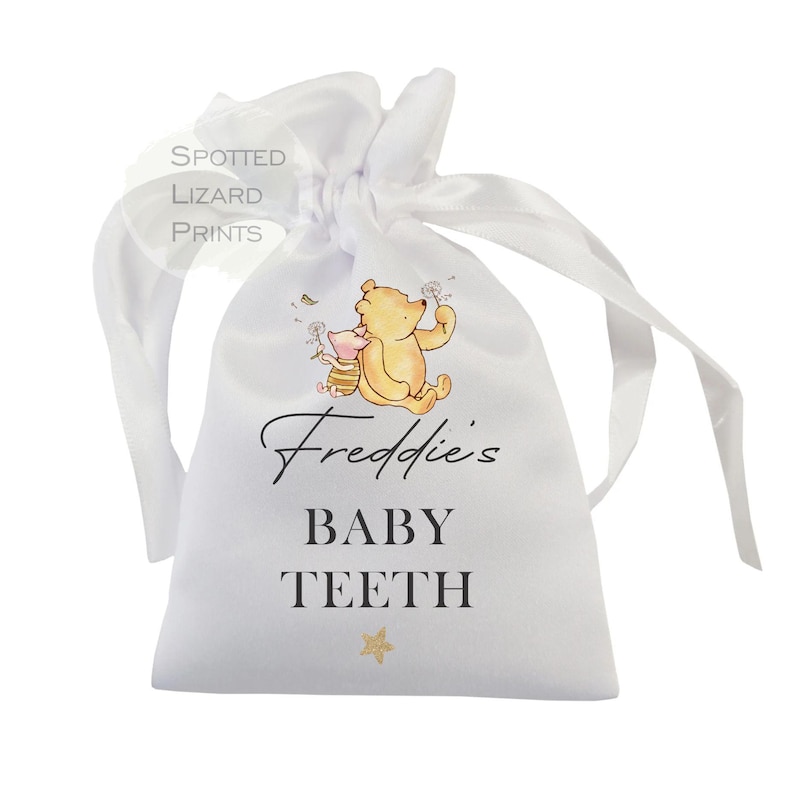 May include: White satin drawstring bag with Winnie the Pooh and Piglet characters. The bag has the text "Freddie's Baby Teeth" printed on it.