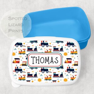 May include: A white lunchbox with a blue lid. The lunchbox features a colourful design of trains and the name "THOMAS" printed on the front.