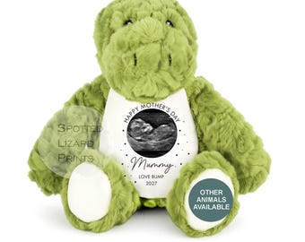 May include: A plush green dinosaur toy with a white belly panel featuring a black and white ultrasound image. The text reads: HAPPY MOTHER'S DAY, Mummy, LOVE BUMP, 2027. The dinosaur has a textured, soft fabric finish and white patches on its feet.