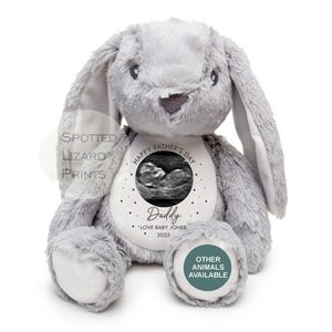 May include: Gray plush bunny with a white circle on its chest. The circle has a black and white ultrasound image inside, with the text "Happy Father's Day" above the image and "Daddy" below the image. The text "* 'Love Baby Jones 2025" is below the word "Daddy". A smaller circle on the bunny's foot has the text "Other Animals Available".