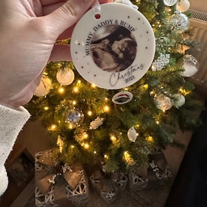 Może przedstawiać: Okrągła biała ceramiczna ozdoba świąteczna z czarno-białym zdjęciem USG pośrodku. Tekst głosi MUMMY, DADDY & BUMP oraz Christmas 2023. Ozdoba zawieszona jest na białej wstążce i ozdobiona małymi czarnymi gwiazdkami.