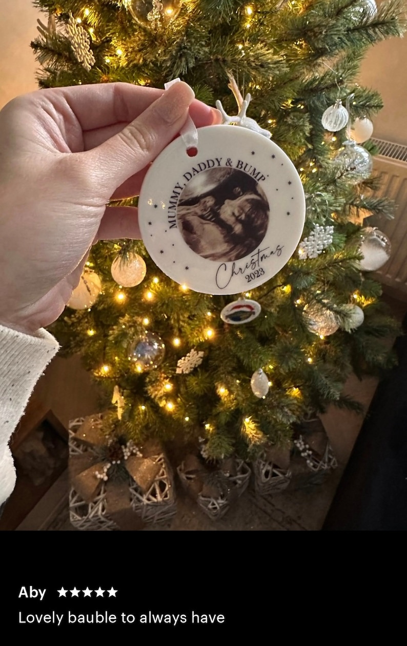 Może przedstawiać: Okrągła biała ceramiczna ozdoba świąteczna z czarno-białym zdjęciem USG pośrodku. Tekst głosi MUMMY, DADDY & BUMP oraz Christmas 2023. Ozdoba zawieszona jest na białej wstążce i ozdobiona małymi czarnymi gwiazdkami.
