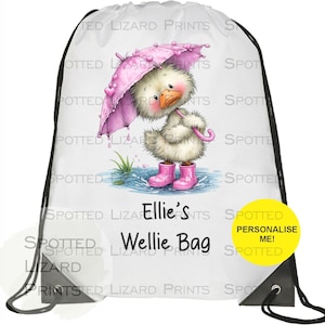 Puede incluir: Bolsa de cordón blanca con un patito de dibujos animados con botas de agua rosas y un paraguas rosa. La bolsa tiene el texto "Ellie's Wellie Bag" y una pegatina amarilla "Personalise Me!"