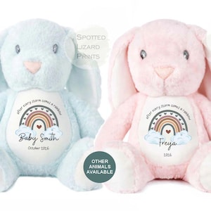 May include: Two plush stuffed bunnies, one light blue and one light pink, each featuring a white belly patch with a printed rainbow graphic, the text "after every storm comes a rainbow," and personalised names "Baby Smith" and "Freya" with dates.