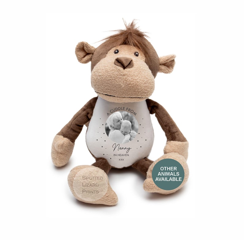 May include: A brown and tan plush monkey toy with a white belly featuring a circular black and white photograph of an adult and a baby. The text reads A CUDDLE FROM Nanny IN HEAVEN XXX. A circular teal badge on the foot says OTHER ANIMALS AVAILABLE.
