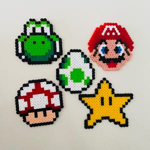 Könnte beinhalten: Eine Sammlung farbenfroher Pixel-Art-Charaktere aus der Super Mario-Videospielserie. Enthält Marios Gesicht, einen Yoshi-Charakter, einen Pilz, einen Stern und ein Ei. Jeder Charakter besteht aus kleinen, farbigen Perlen.