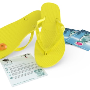Könnte beinhalten: Ein Paar leuchtend gelbe Flip-Flops mit einem kleinen orangefarbenen und weißen Etikett, das an einem Riemen befestigt ist. Die Flip-Flops liegen auf einer weißen Oberfläche mit einer kleinen Karte, auf der "So Easy" steht und ein QR-Code abgebildet ist.