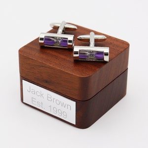 May include: A pair of silver cufflinks with purple hourglass inserts in a wooden box with the inscription "Jack Brown Est. 1999".