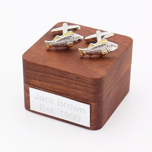 May include: A pair of silver and gold fish cufflinks in a wooden box with the inscription "Jack Brown Est. 1999".