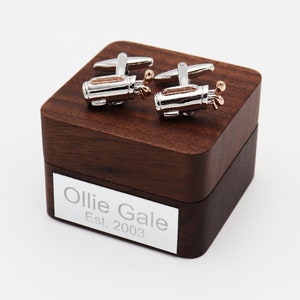 Può includere: Un paio di gemelli d'argento a forma di sacca da golf con dettagli in oro rosa, in una scatola di legno con l'iscrizione "Ollie Gale Est. 2003".