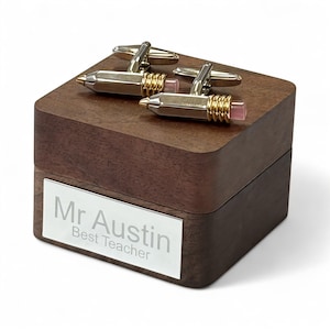 Puede incluir: Gemelos dorados y plateados con forma de lápiz, sobre una caja de madera oscura. Los gemelos tienen detalles rosas y se exhiben en una caja con una placa plateada que dice "Mr Austin Best Teacher". Un regalo para un profesor.