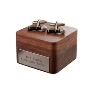 Könnte beinhalten: Eine dunkle Holzbox mit einem silbernen Namensschild mit der Aufschrift "No 1: Daddy Love from Nathan". Zwei Paar silberne und schwarze Manschettenknöpfe mit Kristallkugel-Design liegen oben auf.