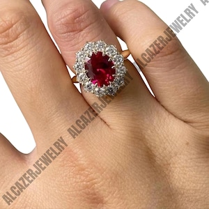 Peut inclure: Une bague en or ornée d'un grand rubis de forme ovale, entouré d'un halo de petits diamants clairs. La bague est montée sur un anneau en or et portée sur une main.