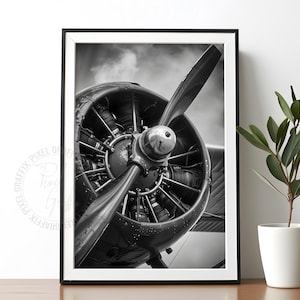 May include: A black and white framed wall art print featuring a close-up view of a vintage radial aircraft engine with a prominent propeller blade. The image captures the intricate mechanical details of the engine cylinders and the metallic hub.