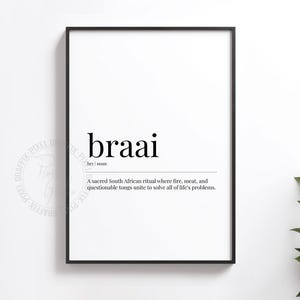 May include: A framed print featuring the word "braai" in black, with a definition below. The definition describes a South African ritual involving fire, meat, and tongs. The print is in a black frame against a white background.