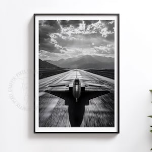 May include: Black and white framed print of a jet fighter taking off on a runway. The image captures the aircraft in motion, with blurred streaks indicating speed. Mountains and a cloudy sky form the backdrop, creating a dramatic aviation scene.
