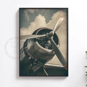 May include: A framed wall art print featuring a close-up view of a vintage silver airplane engine and propeller against a cloudy sky. The metallic engine casing shows detailed mechanical components, and the propeller blades are angled forward.