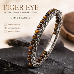 May include: A bracelet featuring a strand of brown and gold tiger eye natural stone beads paired with a silver-toned stainless steel woven chain. The piece includes a smooth, polished magnetic clasp and is labelled with text including TIGER EYE.