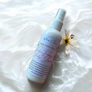 Puede incluir: Un frasco de spray de loción corporal blanco con una etiqueta que dice "Vanilla Velvety Jasmine". El frasco está junto a una flor blanca con detalles amarillos. La loción está perfumada con aceite de almendras, jazmín, fresia y glaseado de vainilla.