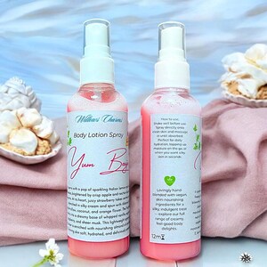 May include: Two pink body lotion spray bottles with white labels. The labels read "Willows Charms Body Lotion Spray Yum Boy" and include product details. The bottles are on a pink cloth with decorative pastries.