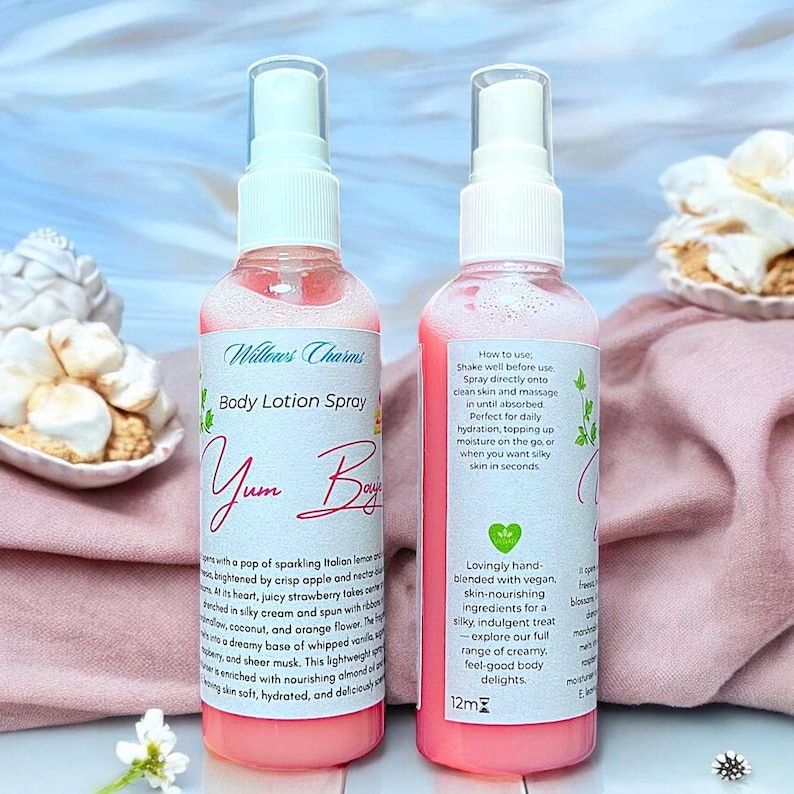 May include: Two pink body lotion spray bottles with white labels. The labels read "Willows Charms Body Lotion Spray Yum Boy" and include product details. The bottles are on a pink cloth with decorative pastries.