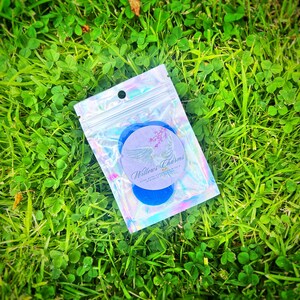 May include: A small iridescent zippered bag containing two blue round charms with a white circle sticker on one charm. The sticker has the text "Willow's Charms" and "Hand Made Charms with a Sprinkle of Love".